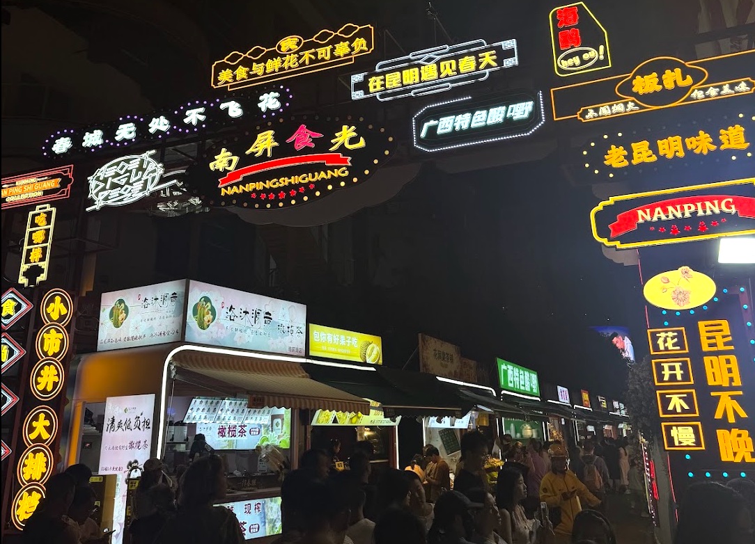 Nanping Street in Kunming bei Nacht — beleuchtete Neon-Schilder über Garküchen und Streetfood-Ständen