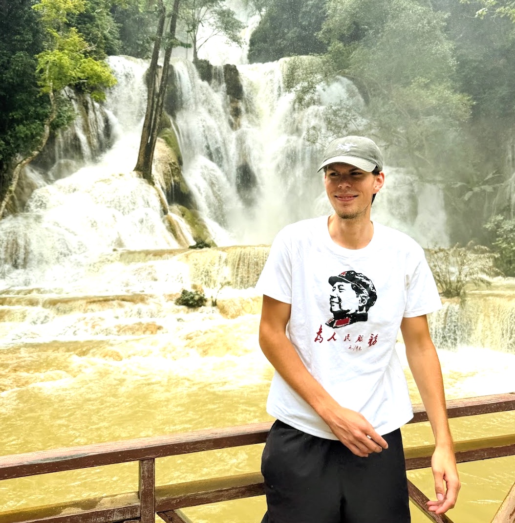 Kevin vor dem Kuang Si Wasserfall bei Luang Prabang, türkis-braunes Wasser kaskadiert über mehrere Stufen