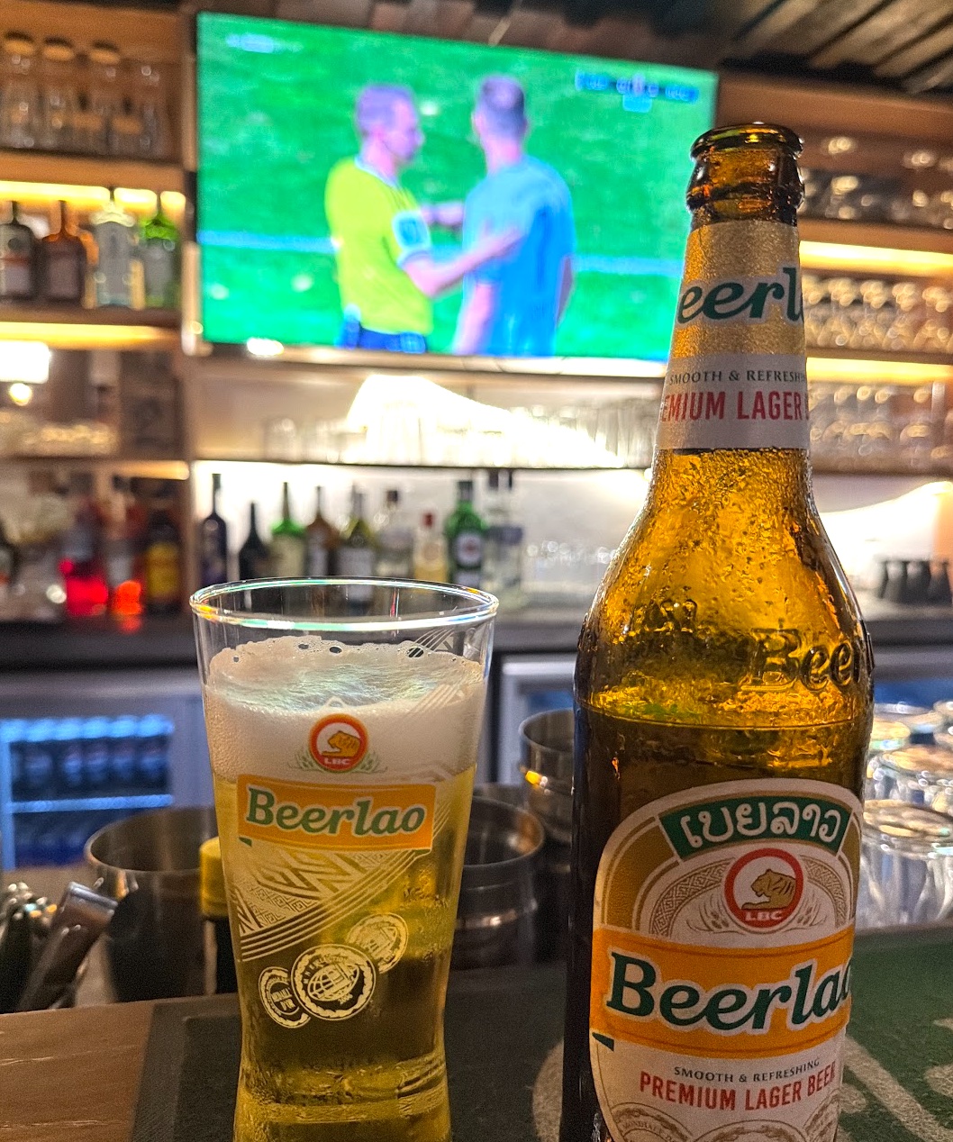 Beerlao im Glas und in der Flasche in der Outback Bar in Luang Prabang, im Hintergrund läuft ein Fußballspiel auf dem Fernseher
