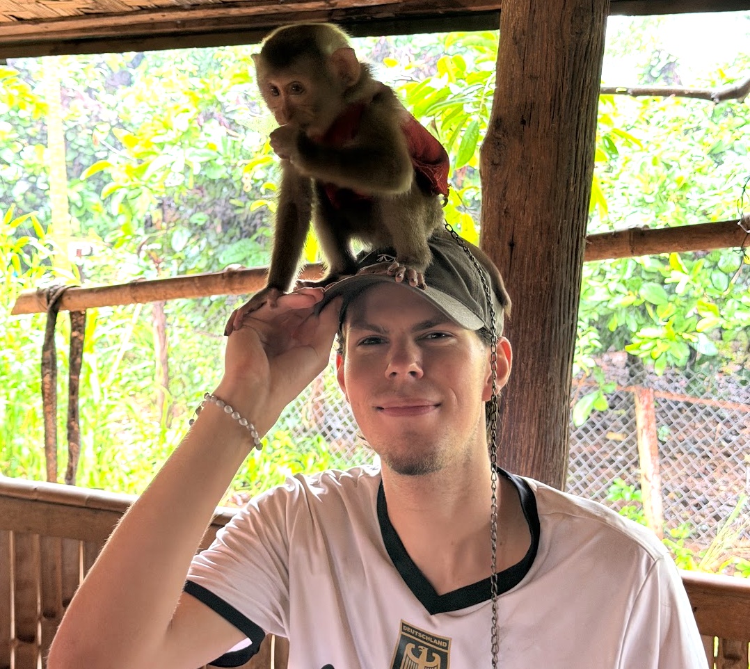 Der zahme Affe England sitzt auf Kevins Käppi bei Captain Hook's Homestay auf dem Bolaven-Plateau