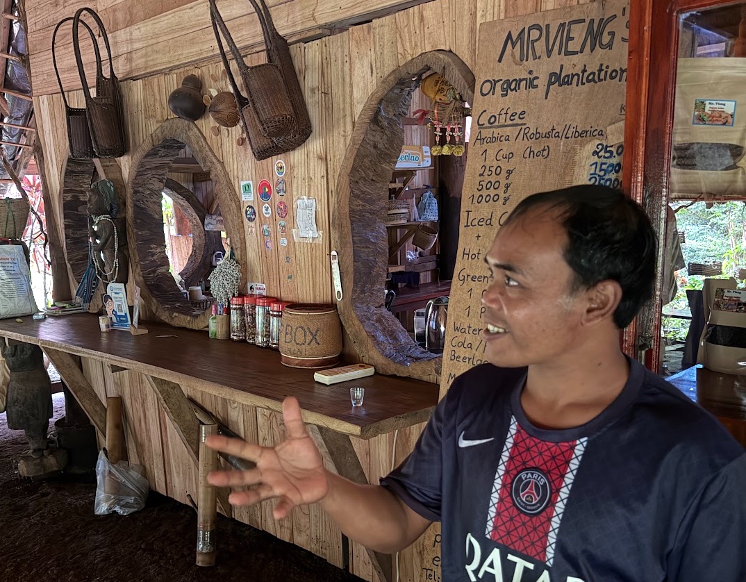 Mr. Vieng erklärt seine Kaffeeplantage, im Hintergrund die Theke mit Preisschild seiner Organic Plantation