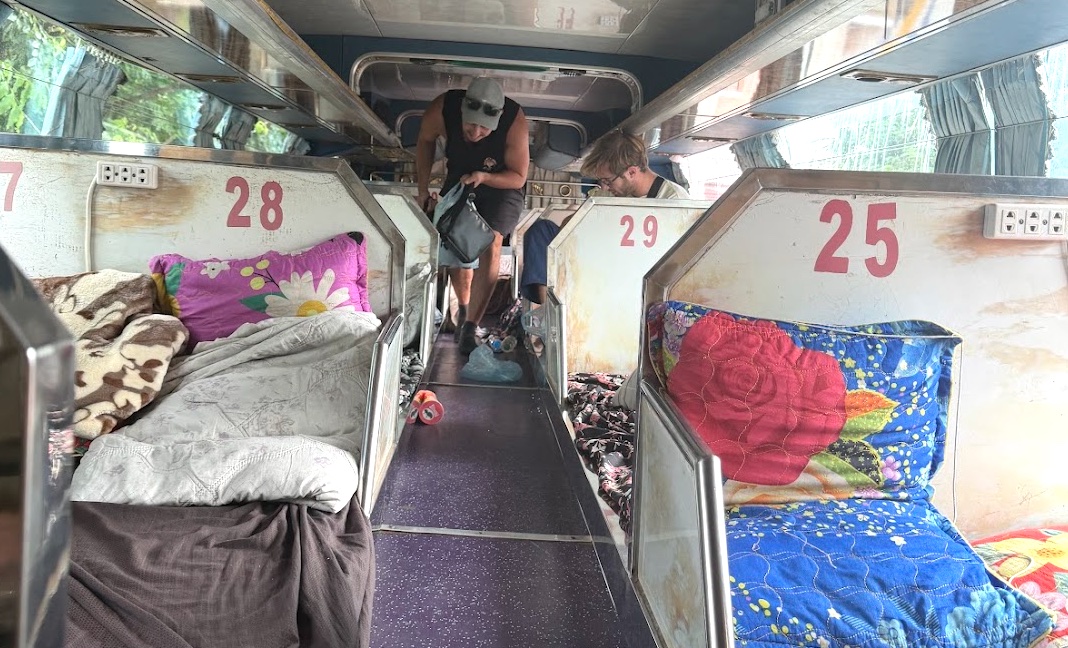 Enge Doppelbett-Schlafplätze im Nachtbus Richtung Pakse, nummerierte Liegen mit bunten Decken