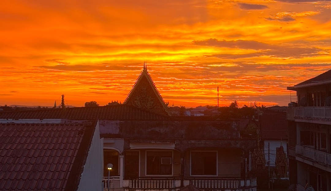 Feuerroter Sonnenuntergang über den Dächern von Pakse, Blick vom Sanga Rooftop Hostel auf einen Tempelgiebel
