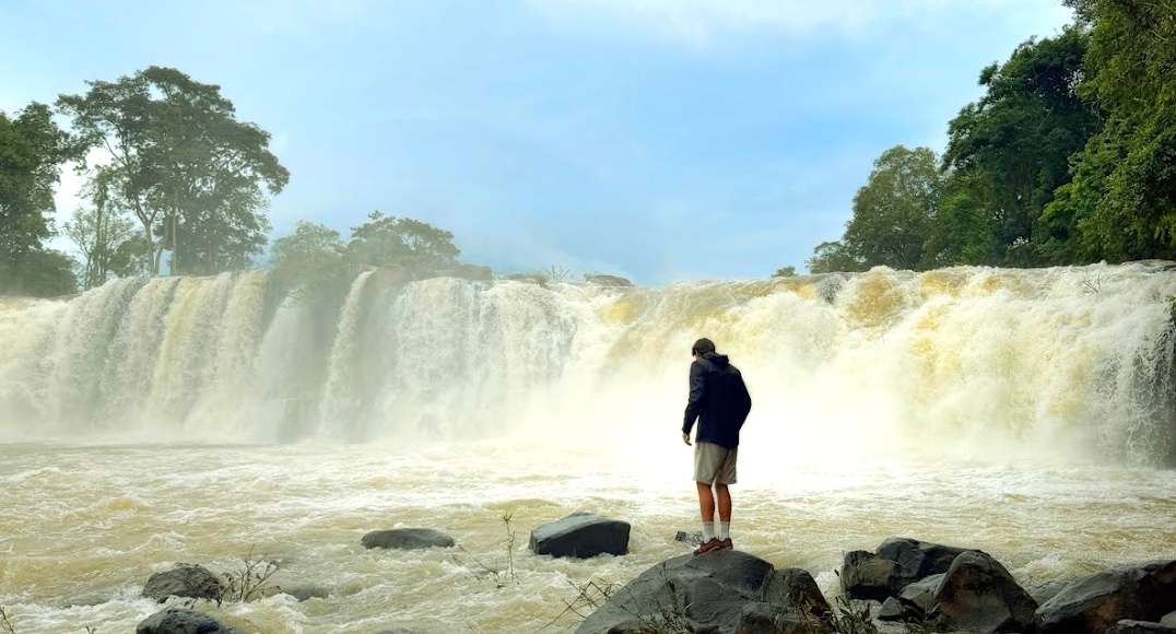 Kevin steht auf Felsen vor dem breiten Tad Koo Wasserfall auf dem Bolaven-Plateau