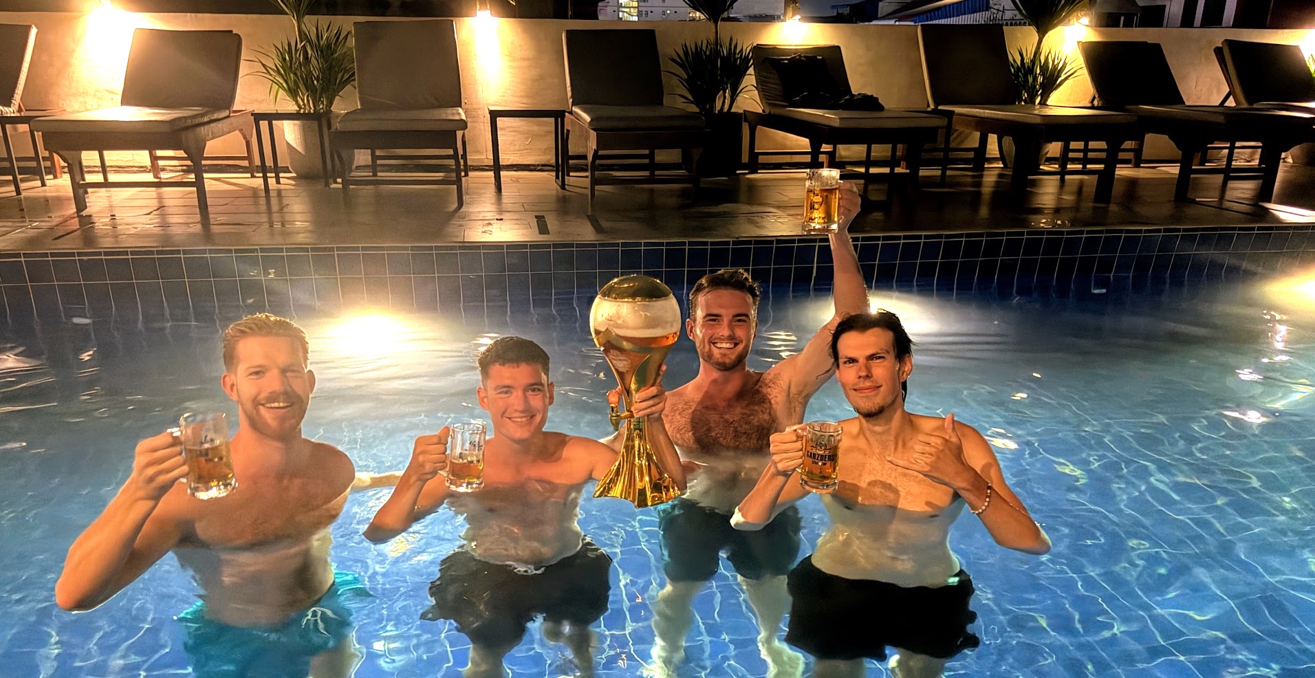 Kevin, Matt, Hayden und Leo stehen nachts im Pool des Onederz Hostel und stoßen mit Bierkrügen und einem goldenen Bierturm an