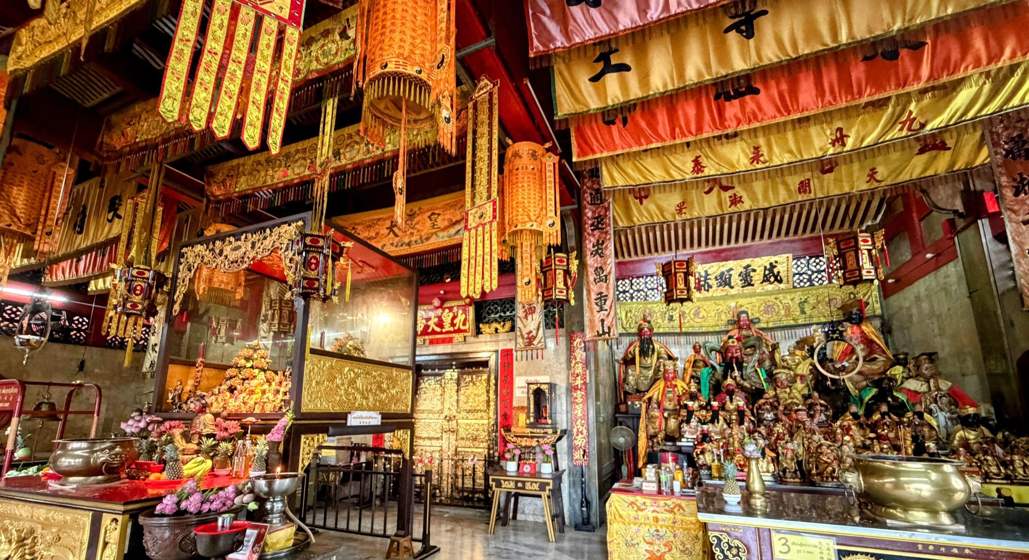 Innenraum des Jui Tui Shrine in Phuket Old Town — goldene Statuen, rote Fahnen, Weihrauchspiralen