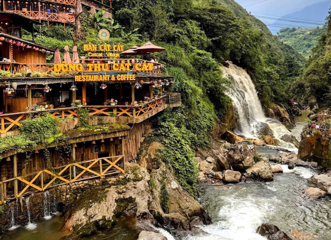 Cat Cat Village bei Sapa — Restaurant auf Stelzen über einem Wasserfall, umgeben von grünen Bergen