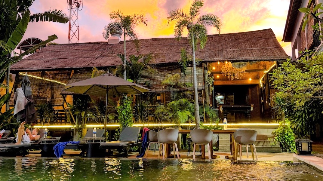 Pool-Bereich des Passport Hostel in Siem Reap bei Sonnenuntergang, Liegestühle und Bar unter einem Reetdach