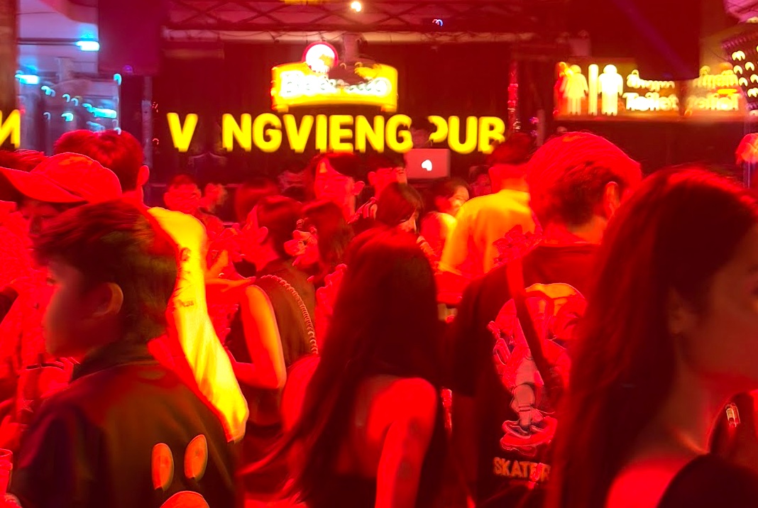 Gedränge im Vang Vieng Pub bei rotem Neonlicht, im Hintergrund das Leuchtschild VANG VIENG PUB
