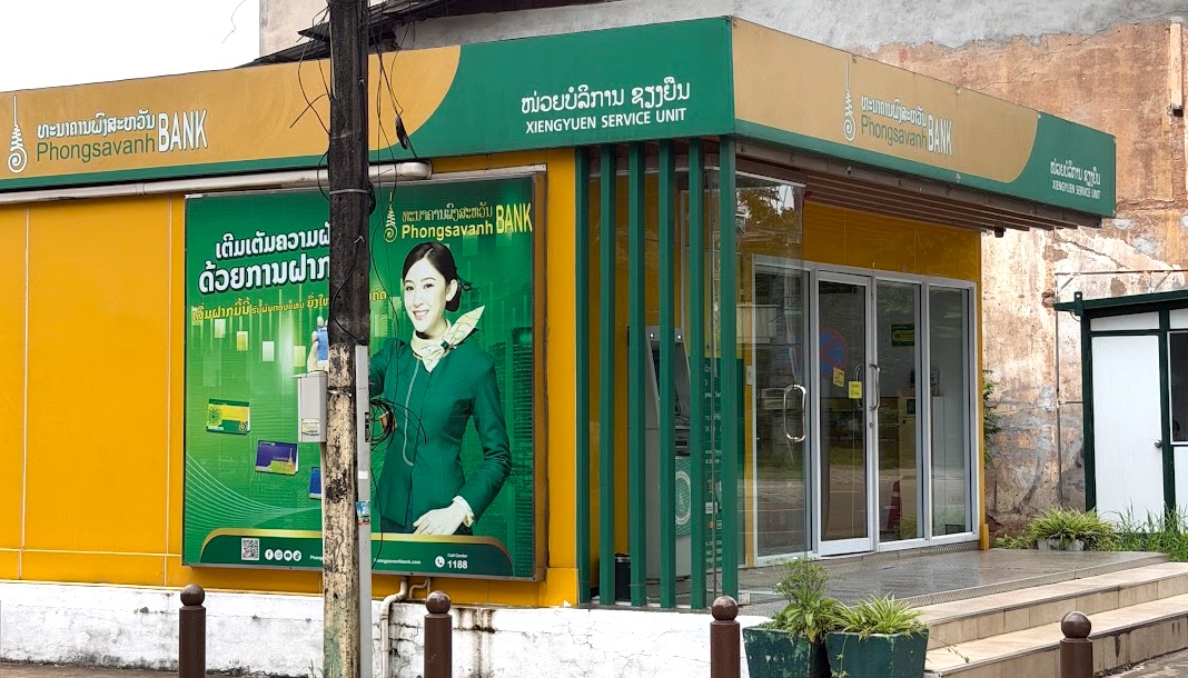Filiale der Phongsavanh Bank in Vientiane, gelb-grüne Fassade mit Werbeplakat und Geldautomat